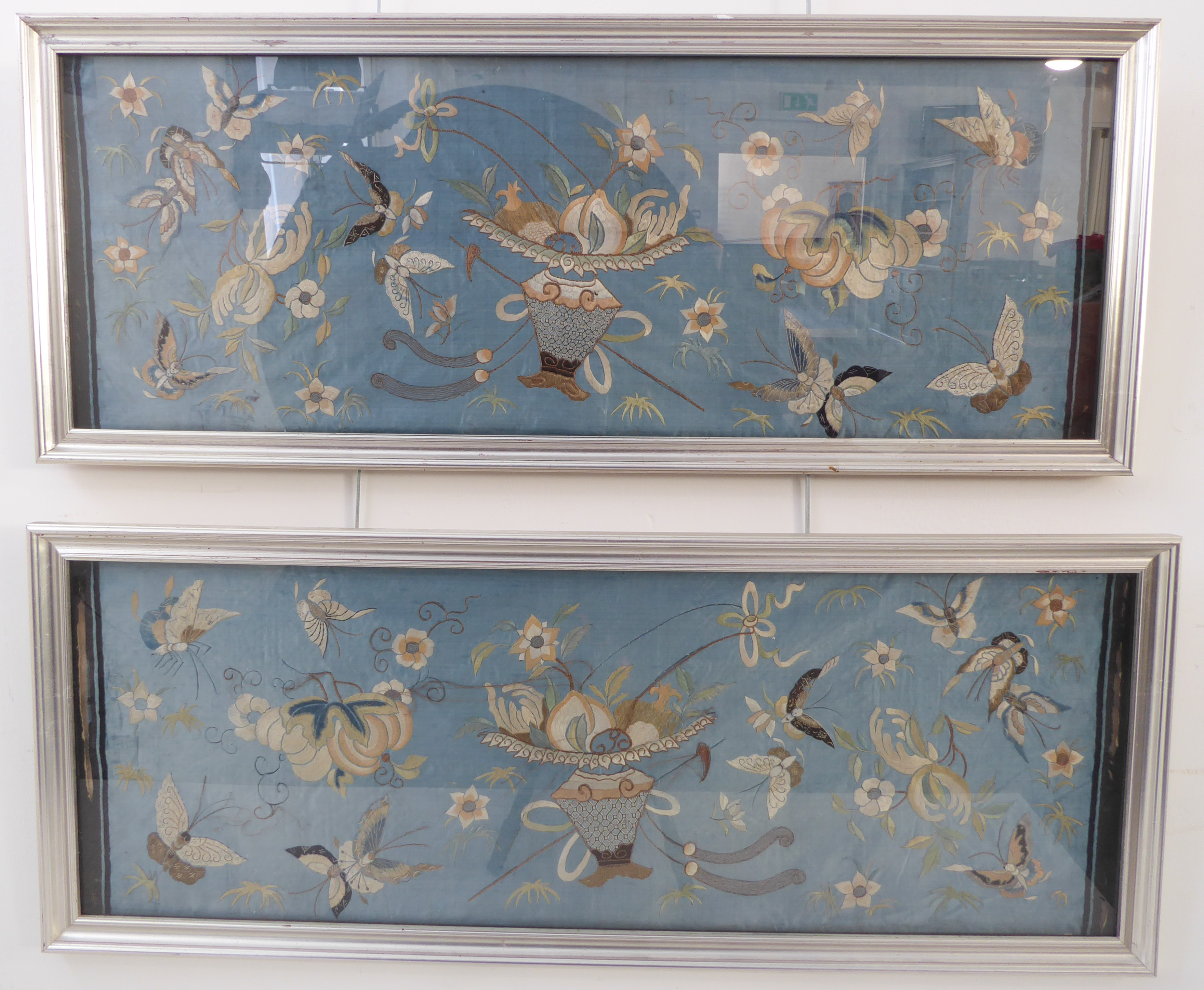 A pair of silver framed and glazed (later) Chinese embroideries on silk: each depicting a central