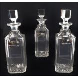 A set of three hand-cut spirit decanters with canted stoppers and corners, and star-cut bases.