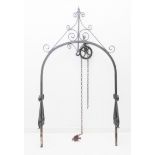 A wrought iron well-head with scrolling pediment above a chain and pulley and with scrolling sides