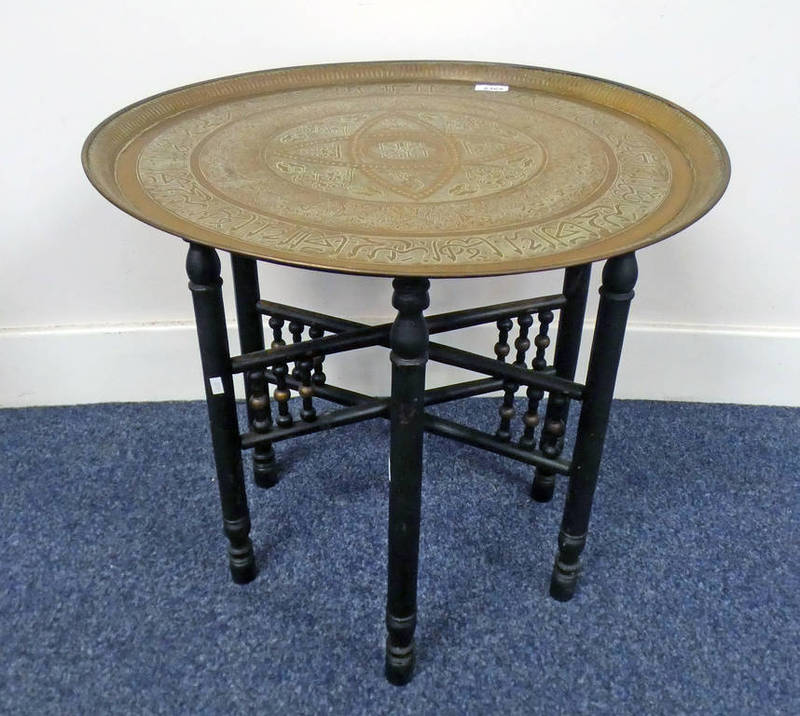 BRASS TRAY TABLE WITH MIDDLE EASTERN EMBOSSED DECORATION ON EBONISED STAND.