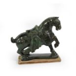 A Chinese Spinach Jade Model of a Horse, in Tang style, with saddle and cloth, one foreleg raised,