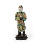 A Chinse Porcelain Figure of a Warrior, Kangxi, standing wearing armour, a box in his right hand,