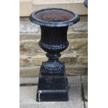 A pair of painted cast iron garden urns of fluted form and raised on spreading square plinths,