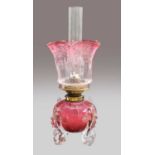 A Victorian cranberry glass oil lamp, the reservoir mounted on four fish shaped feet, with hinks
