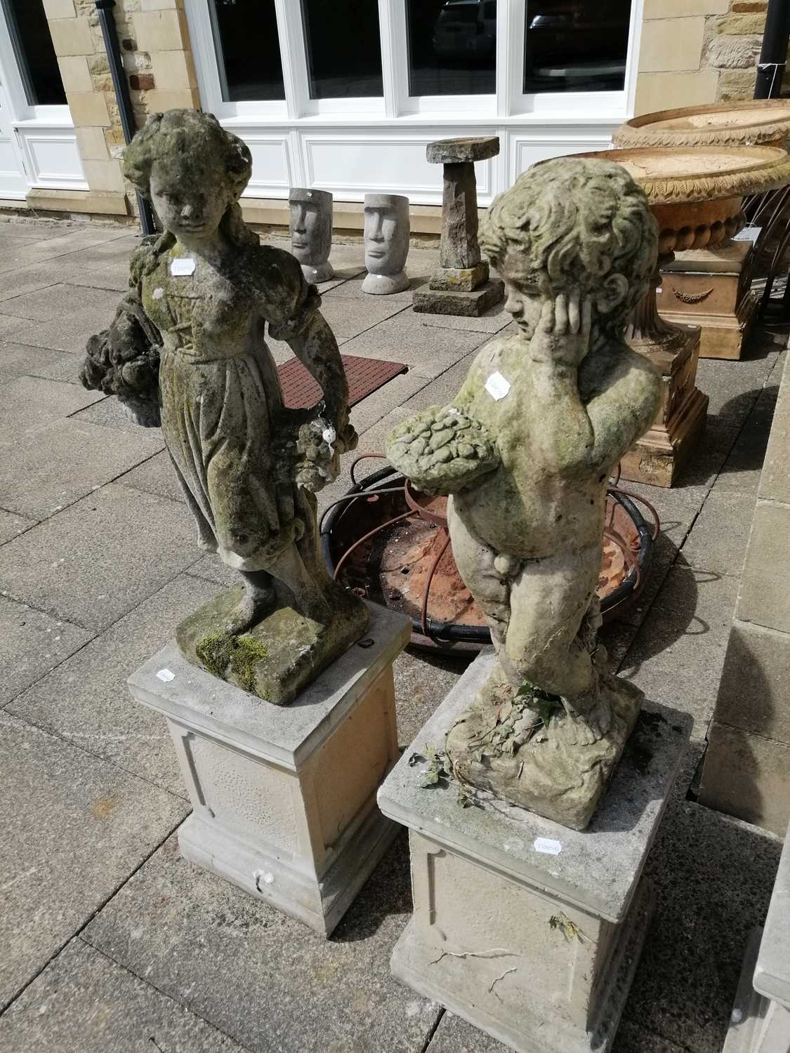 A pair of weathered composition garden statues of children holding flower baskets, on square section