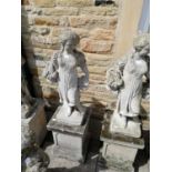A pair of weathered composition garden statues of flower sellers on square section plinth bases,