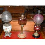 A Cranberry oil lamp and shade, and two othersBoth cranberry lamps, the reservoirs free from