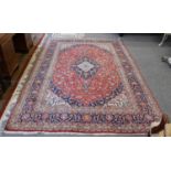 A Kashan Carpet, with a blood red field of scrolling vines centered by an indigo and ivory