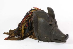 A Chokwe Pig Mask, Angola, of carved wood covered in a dark black/red pigment, with coloured ribbons