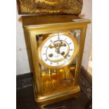 A brass four-glass mantel clock with enamel dial and visible escapement. The movement striking on