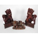 A pair of carved wood Buddhist lions, raised on plinths, approximately 28 cm (h) and one other.