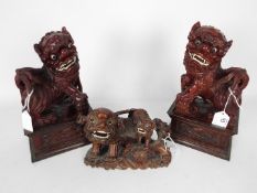 A pair of carved wood Buddhist lions, raised on plinths, approximately 28 cm (h) and one other.