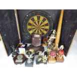 A dartboard in wall mountable cabinet, darts, baseball bat, various sporting trophies.