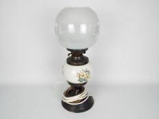 A converted oil lamp with ceramic reservoir with floral decoration and glass shade,