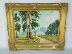 A large framed oil on board landscape scene depicting a path through trees with a mountainous