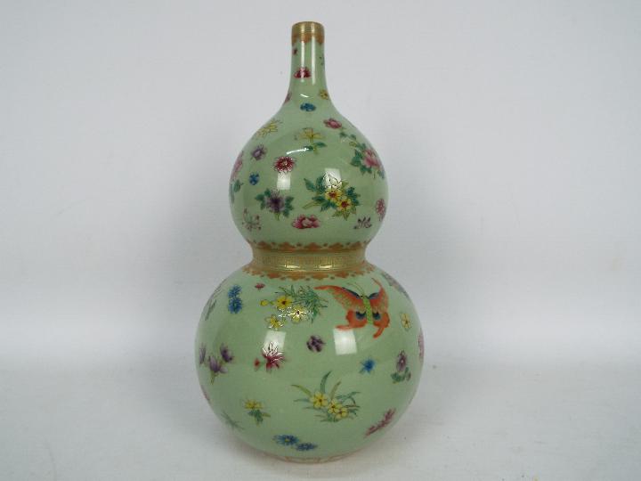 A Chinese double gourd vase decorated with flowers and butterflies against a green ground,