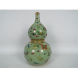 A Chinese double gourd vase decorated with flowers and butterflies against a green ground,