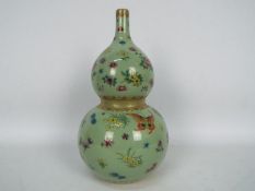 A Chinese double gourd vase decorated with flowers and butterflies against a green ground,