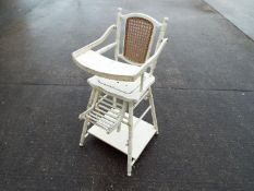 A white painted metamorphic high chair with cane back.