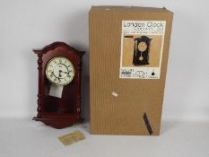 A modern Westminster chime wall clock with key and pendulum, boxed.