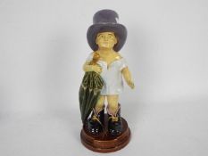 A Brownfield figurine depicting a child wearing his fathers hat and boots and carrying an umbrella,