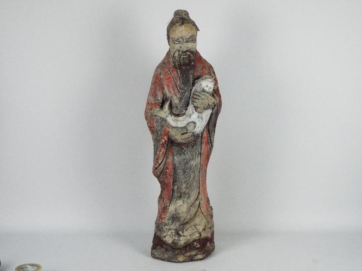 A reconstituted stone garden ornament depicting a Chinese gentleman in flowing robes holding a fish,