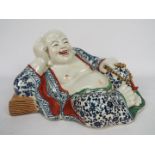 A Chinese ceramic model depicting Budai in reclining pose clutching a string of gilt beads,