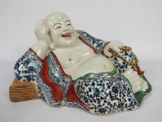 A Chinese ceramic model depicting Budai in reclining pose clutching a string of gilt beads,