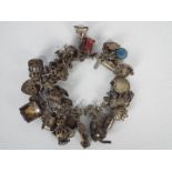 A silver charm bracelet with various silver and white metal charms, padlock clasp and safety chain,