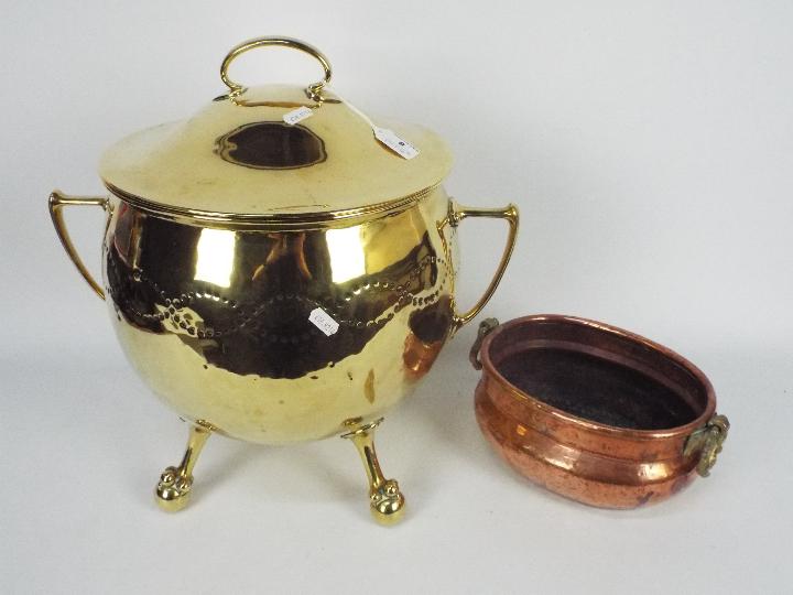 A large, twin handled brass cauldron and cover raised on ball and claw supports,