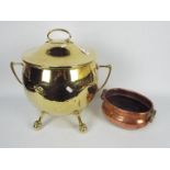 A large, twin handled brass cauldron and cover raised on ball and claw supports,