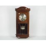 A vintage oak cased wall clock with key and pendulum.