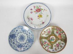 Three plates comprising a Cantonese famille rose example decorated with panels of flowers and
