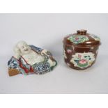 A Chinese ceramic model depicting Budai in reclining pose clutching a string of gilt beads,