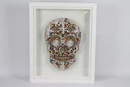 A framed limited edition work depicting a skull decorated with images of £10 notes,
