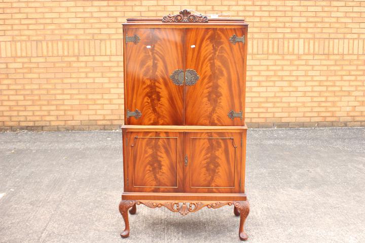 A drinks or cocktail cabinet with mirror backed interior, raise on four supports,