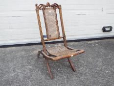 A folding chair with carved decoration, cane seat and backrest.