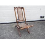 A folding chair with carved decoration, cane seat and backrest.