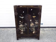 A twin door black lacquered cabinet decorated with perching birds,