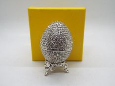 A crystal encrusted egg form trinket box with white enamel interior,