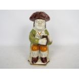 A Prattware Toby jug, depicted seated and holding a foaming jug of ale in the left hand,