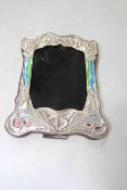 Embossed sterling silver easel photograph frame with enamel decoration, 21cm by 16cm.