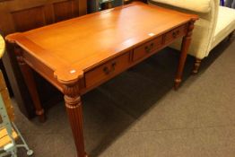 Three drawer writing table on tapering reeded legs, 74cm by 126cm by 66cm.
