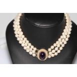 Pearl choker necklace having three strands of uniform pearls with large cabachon amethyst and seed