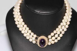 Pearl choker necklace having three strands of uniform pearls with large cabachon amethyst and seed