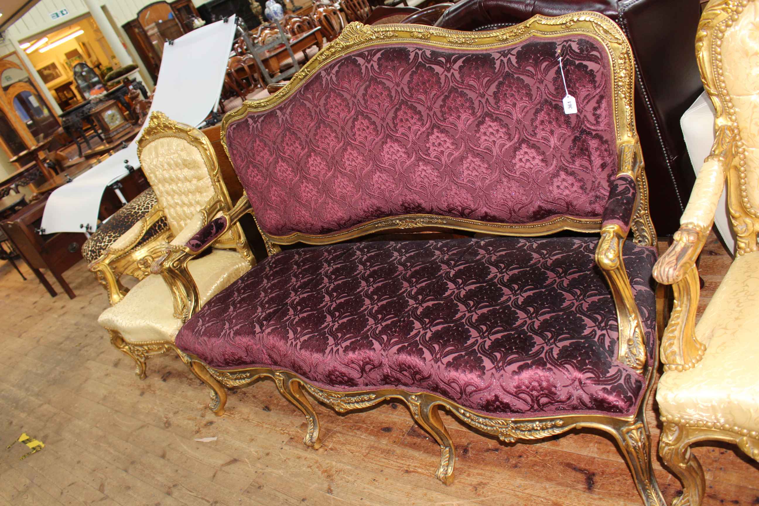 Gilt framed open arm settee with serpentine front seat in dark purple fabric.