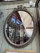 Oval framed wall mirror with ribbon crest, 97cm by 69cm.