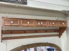 Oak wall rack having five drawers above five brass coat hooks, 41cm by 126cm by 22cm.