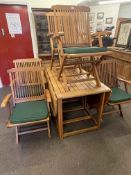 Teak drop leaf garden table and six folding armchairs with seat cushions.