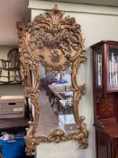Ornate gilt framed wall mirror with cherub decorated crest, 155cm by 69cm.